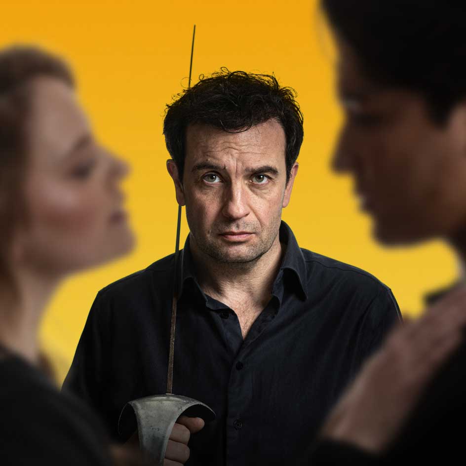 Voorstellingsbeeld van Cyrano: drie personen waarvan een kijkt naar een stel met zwaard in zijn hand, staand voor gele achtergrond.