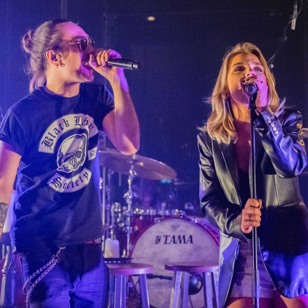 Voorstellingsbeeld van Unplugged Experience: op het podium, man met zonnebril en t-shirt, de vrouw in een donker jasje, neide zingend in microfoons.