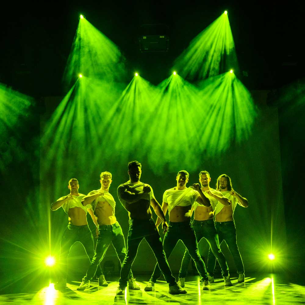 Voorstellingsbeeld van Thunder from downunder: groep dansers op het podium, verlicht door groene schijnwerpers, geeft dramatisch effect tijdens voorstelling.