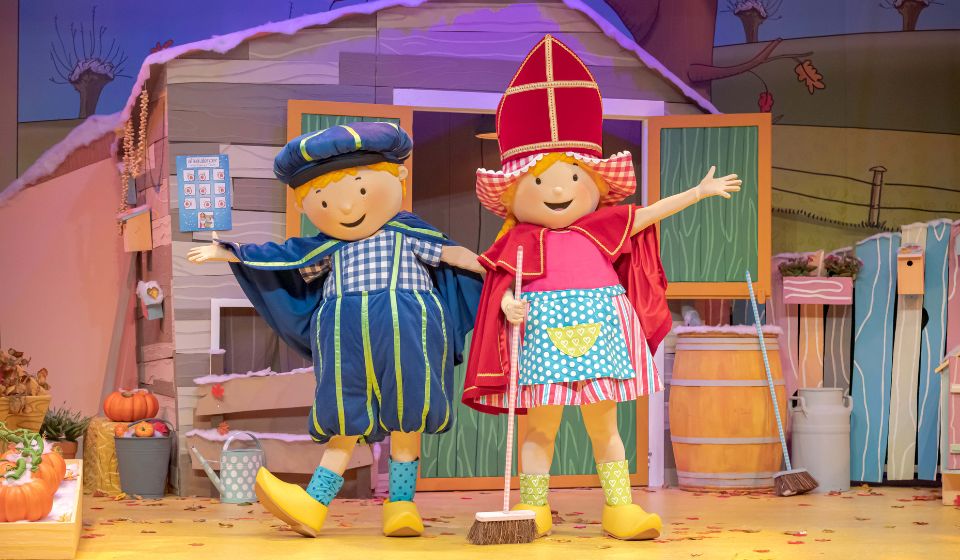 Voorstellingsbeeld van een kindertheater: twee poppen in kleurrijke sinterklaaskostuums op een podium met herfstdecoratie.