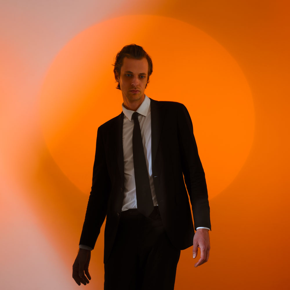 David Linszen in pak voor een feloranje achtergrond met lichtcirkel.