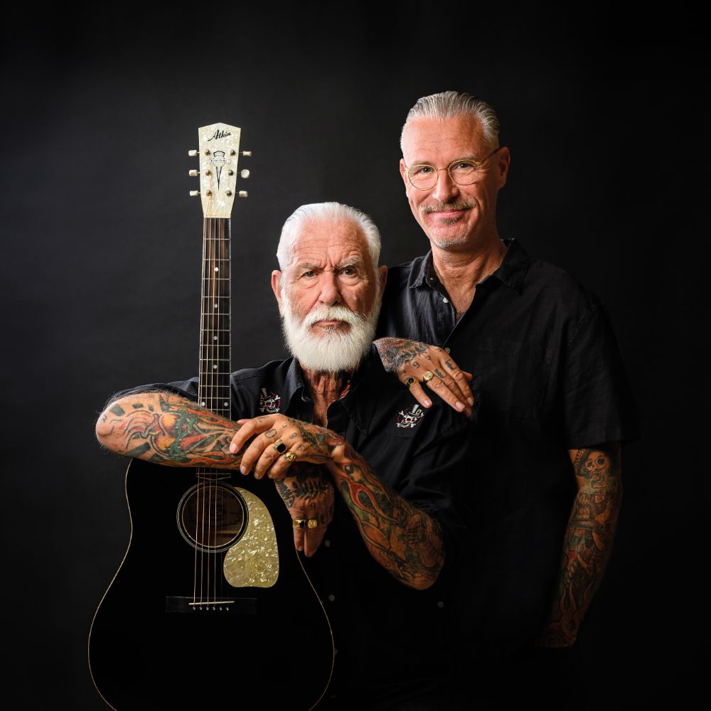 Vader en zoon poseren samen met gitaar voor zwarte achtergrond.