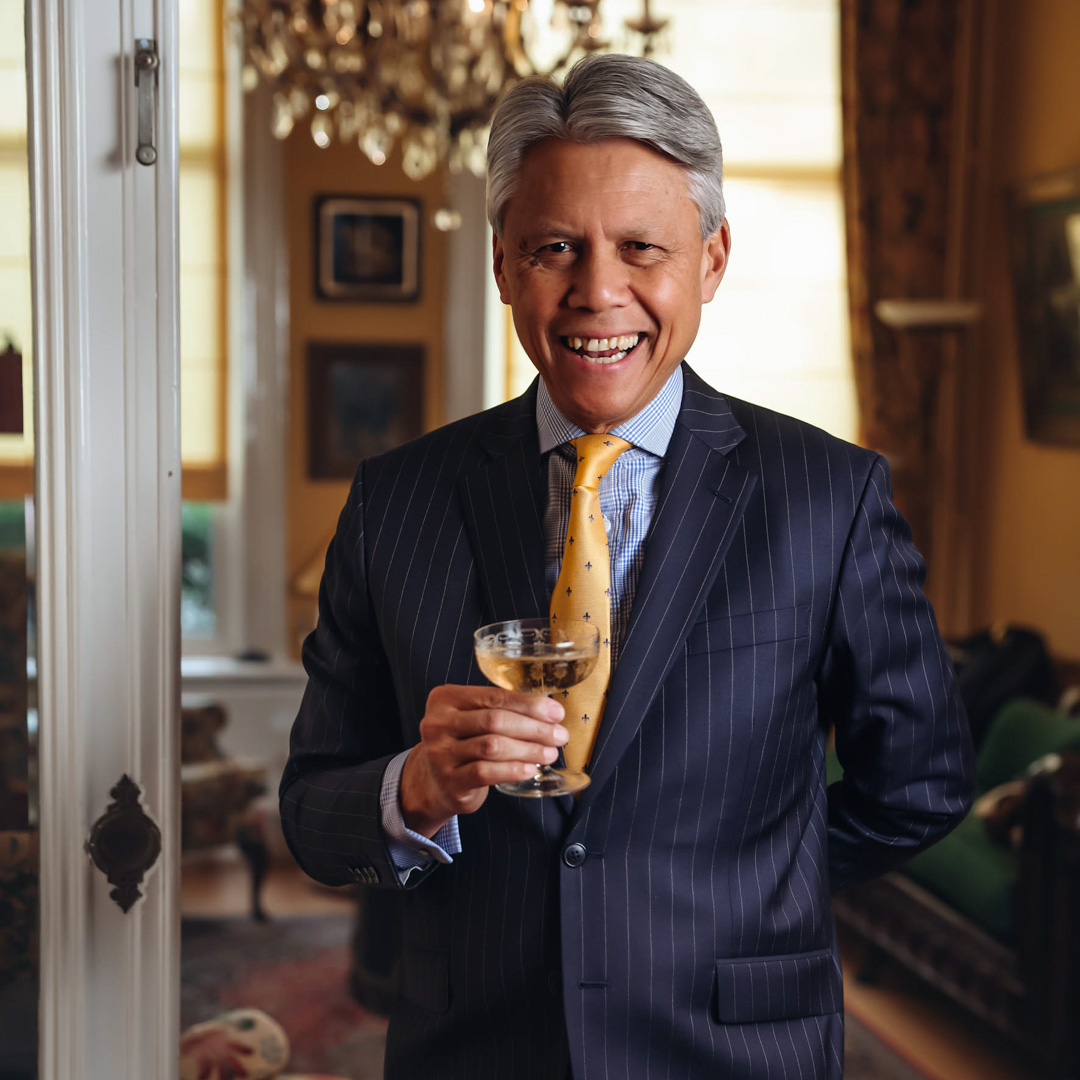 Jan Jaap van Weering is gekleed in pak en glimlacht met een glas wijn in chique woonkamer.