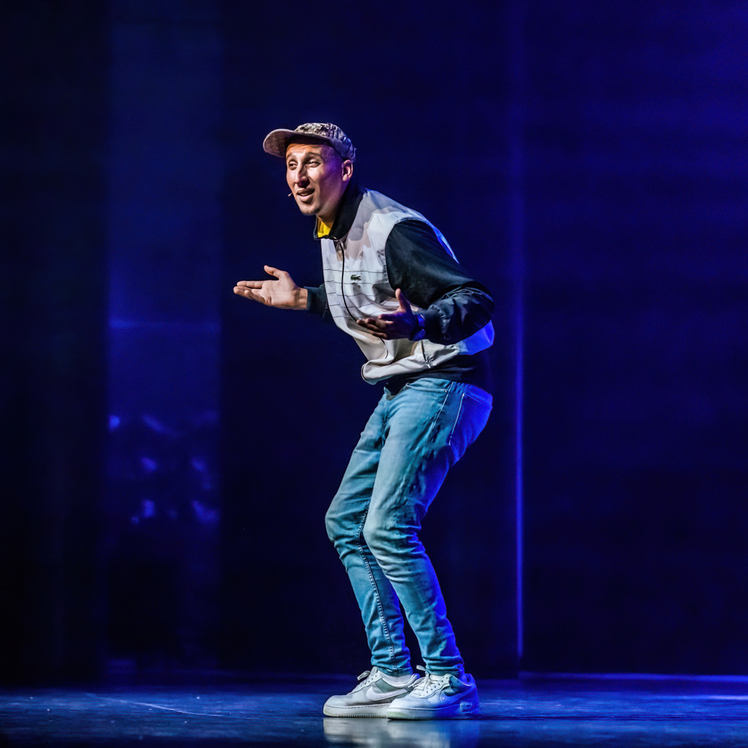 Jawad Es Soufi spreekt energiek op podium in casual outfit met pet.