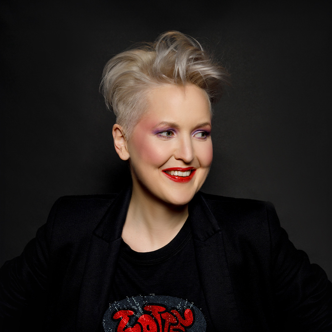 Leonie Meijer lacht met handen in zij, in zwart shirt met rood logo en donkere blazer.