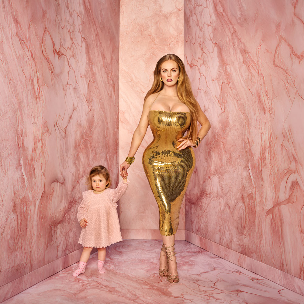 Lisa Ostermann in gouden jurk poseert met jong meisje tegen roze marmerdecor.