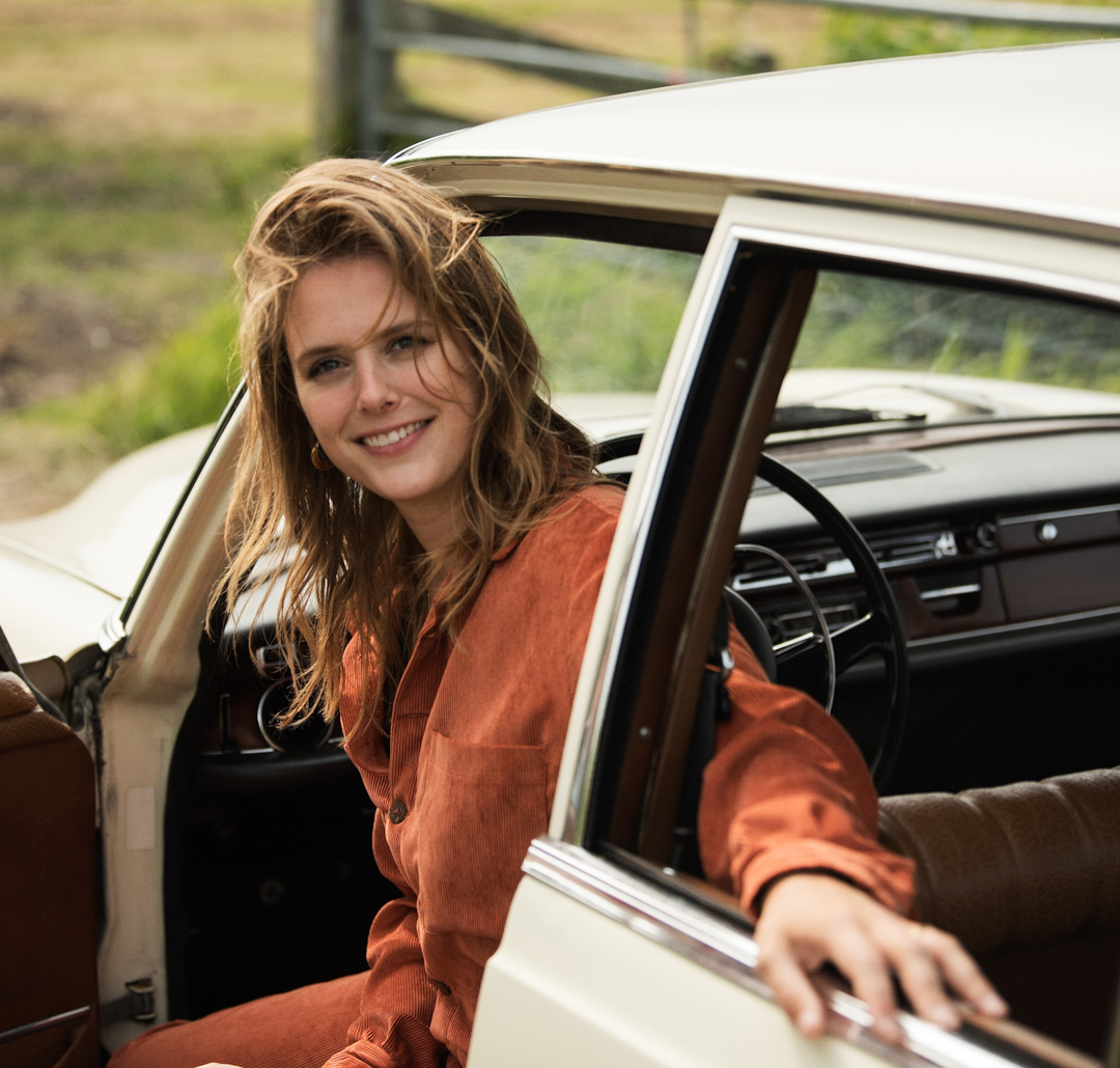 Maaike Ouboter glimlacht terwijl ze uit het raam van een oldtimer kijkt.