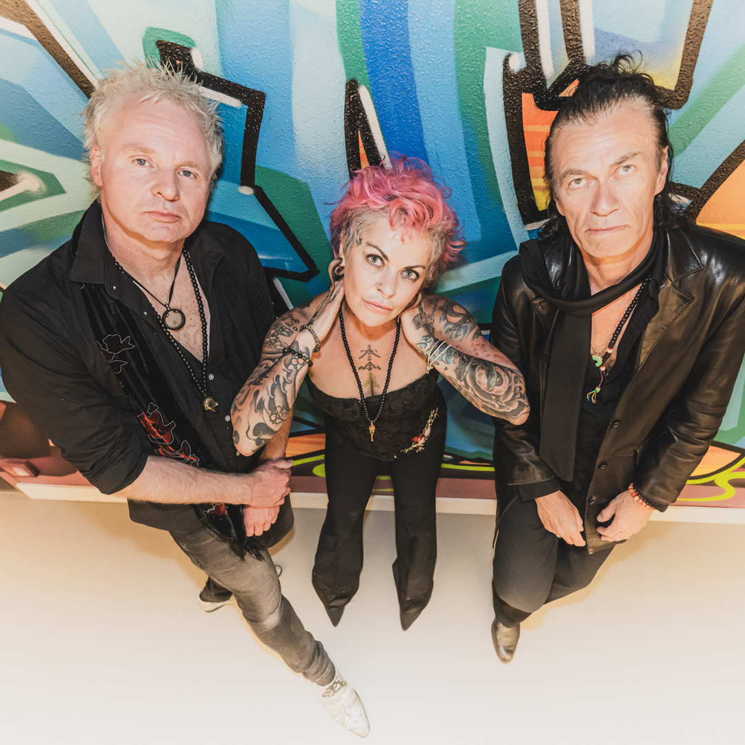 Dilana Smith en ze staat tussen twee muzikanten in leren outfits en achter hen is een graffiti wand.