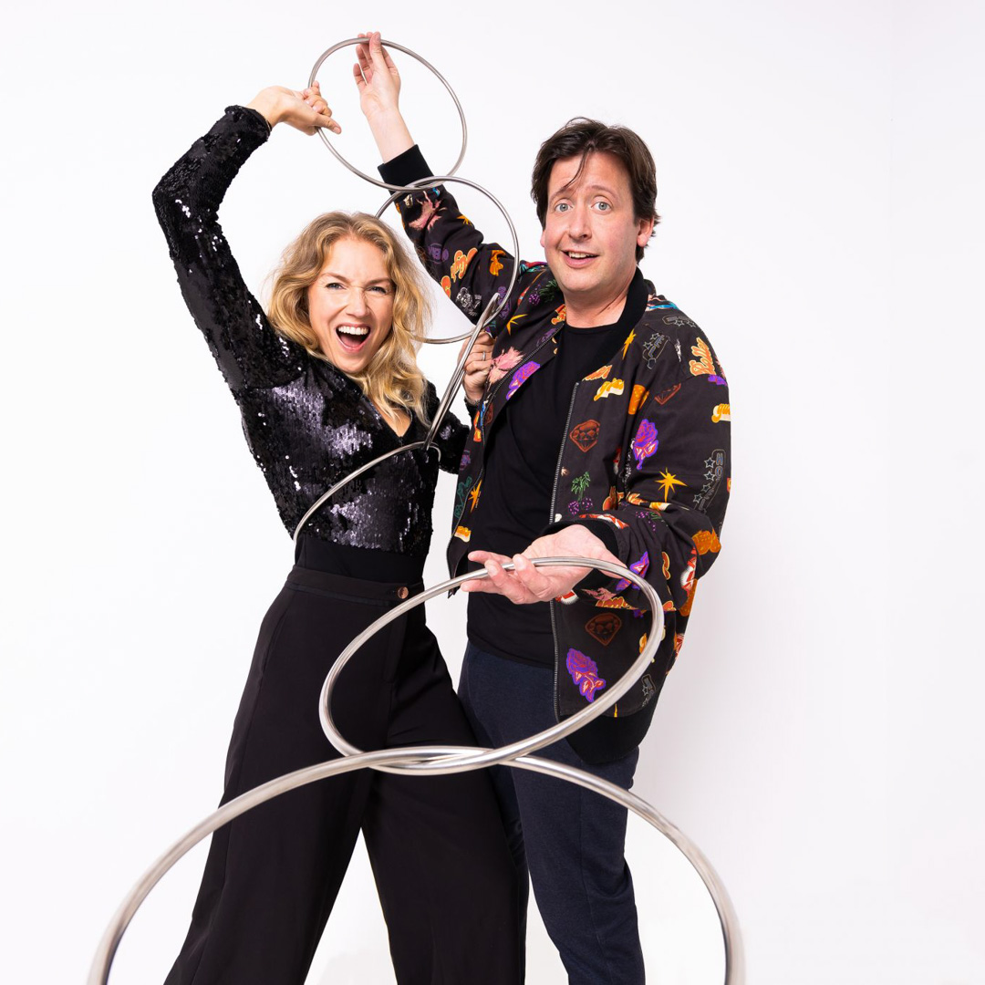 Steven en Jamie lachen en houden metalen ringen speels omhoog in witte studio.