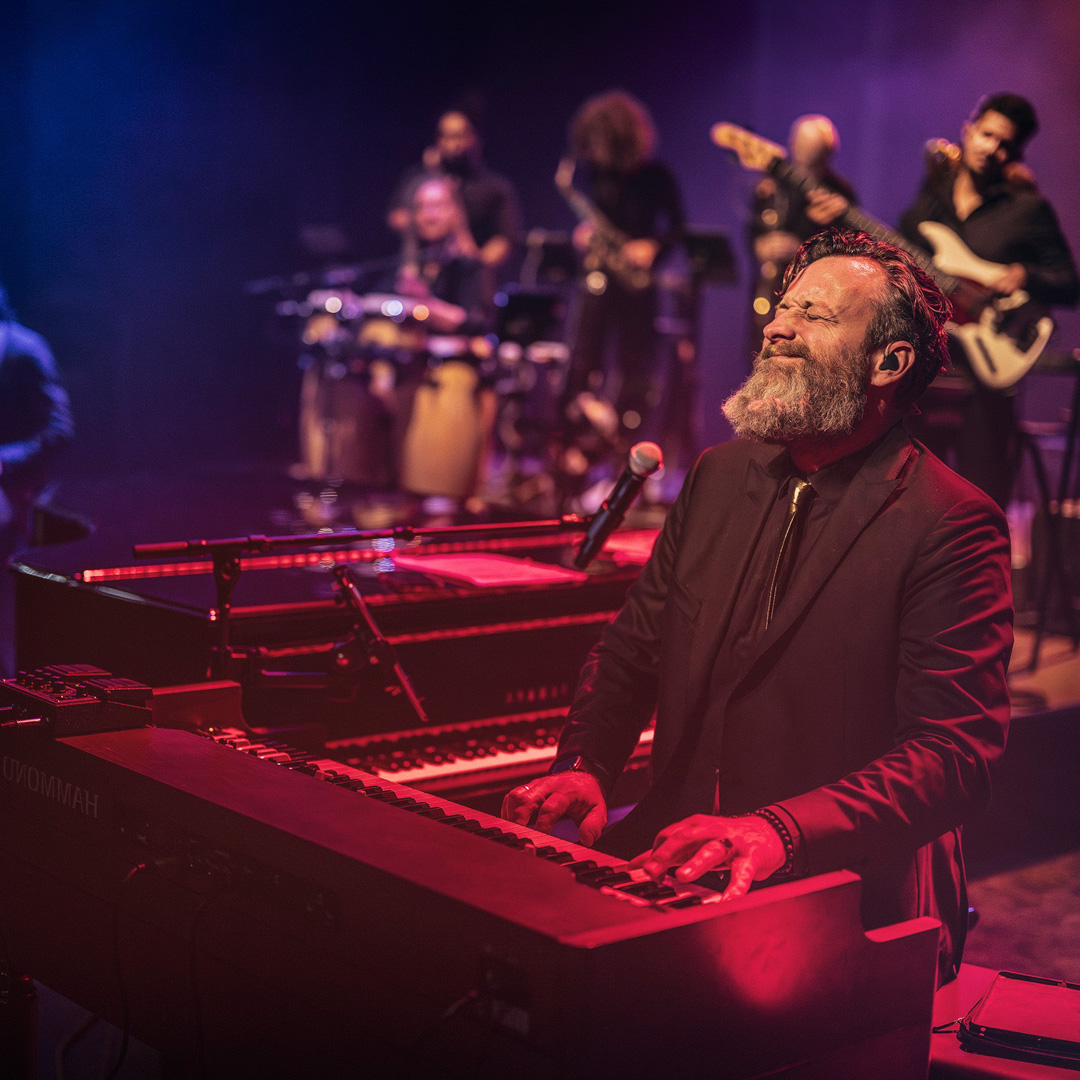 Sven Hammond speelt orgel met gesloten ogen en omringd door bandleden op het podium.