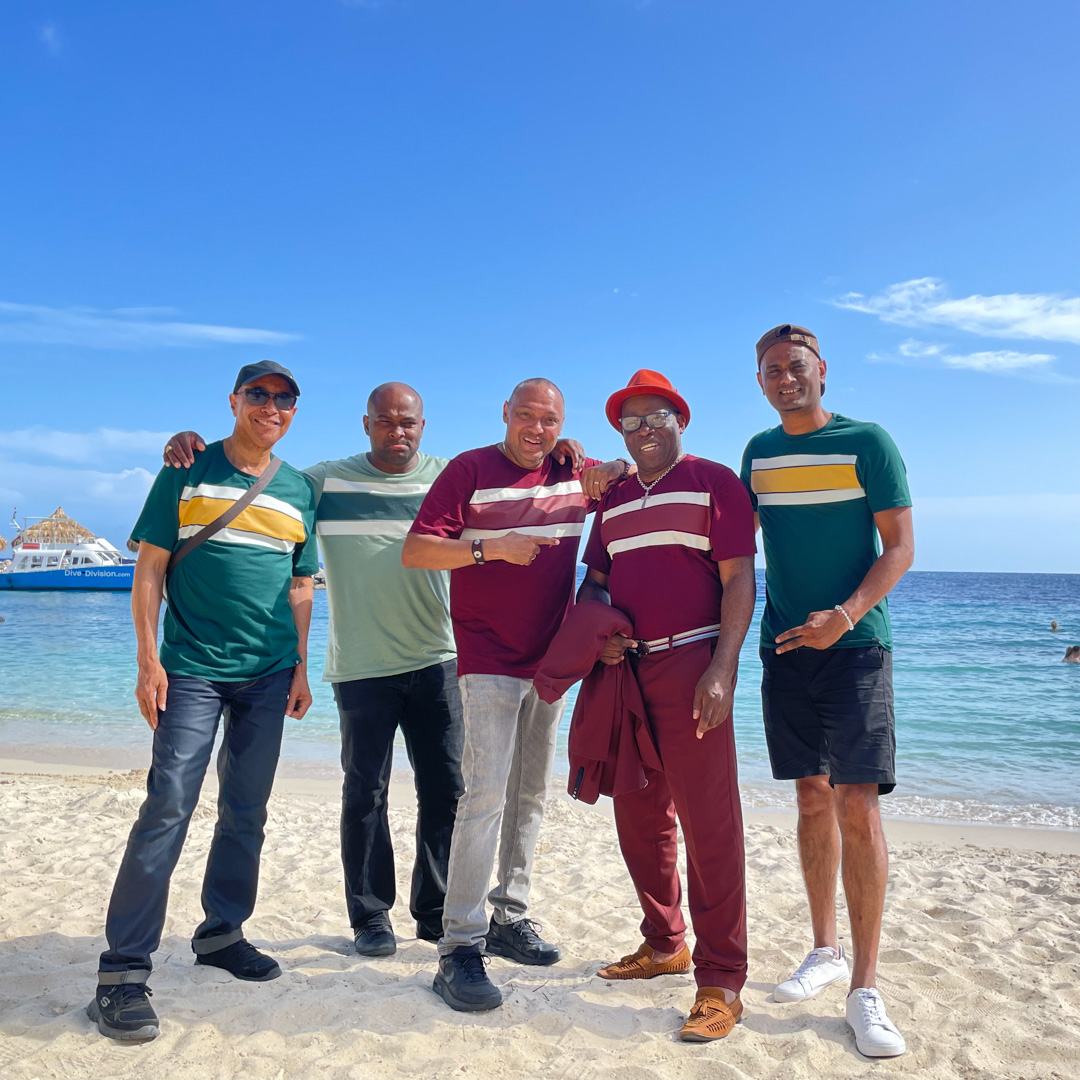 Trafassi leden lachen op tropisch strand met kleurige shirts en blauwe zee op de achtergrond.