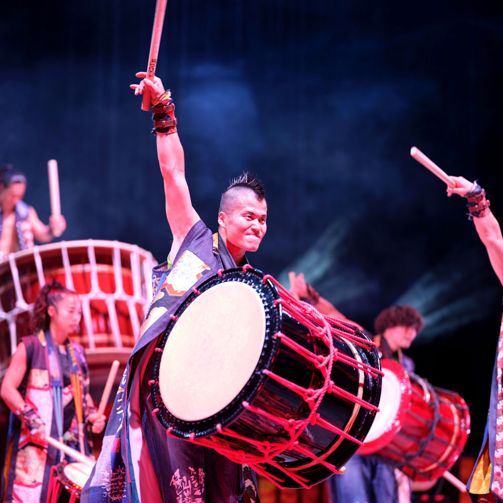 Drummer slaat met kracht op een grote Japanse taiko-drum onder fel podiumlicht.