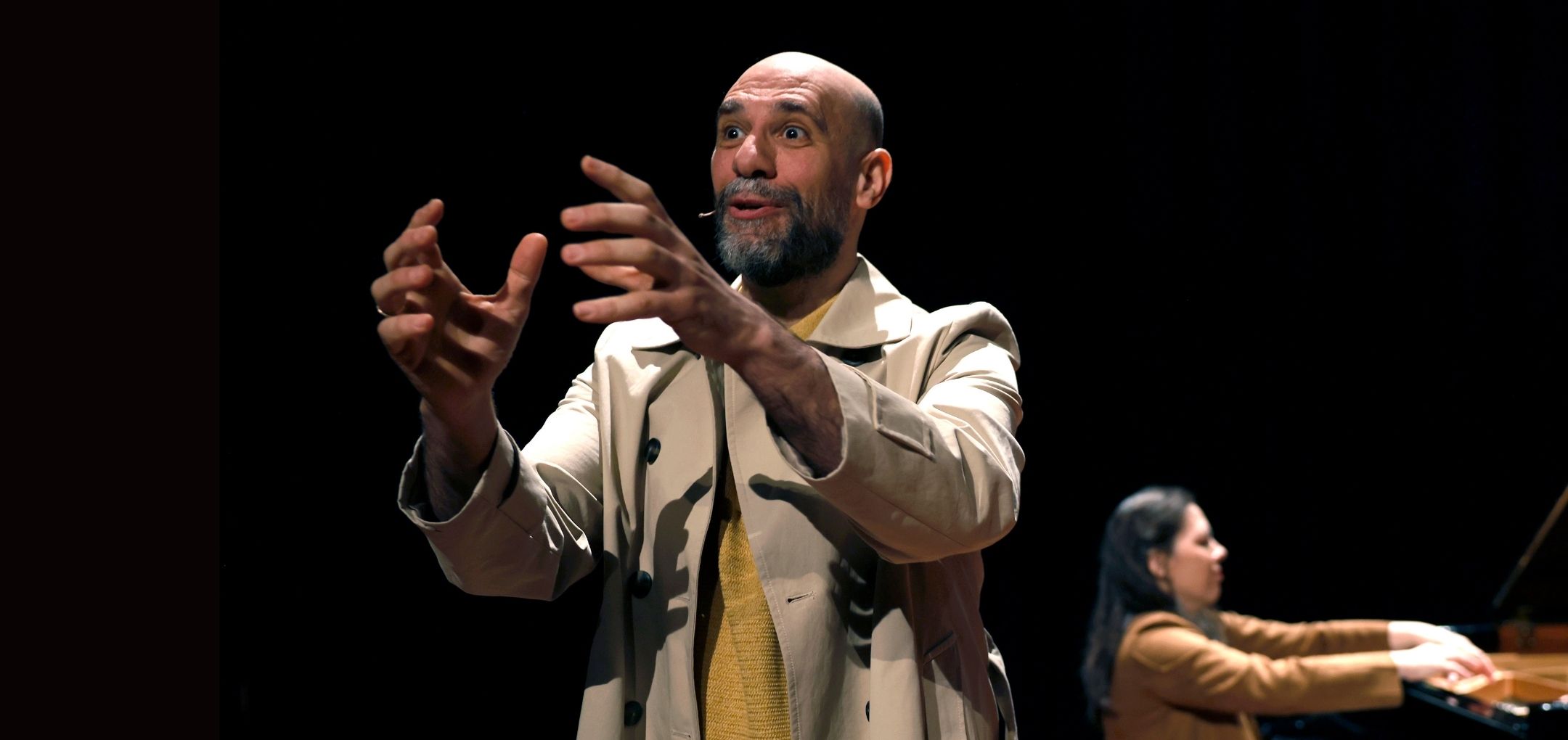 Je ziet Ali in trenchcoat gebaren in spotlicht; Nino speelt piano op de achtergrond.