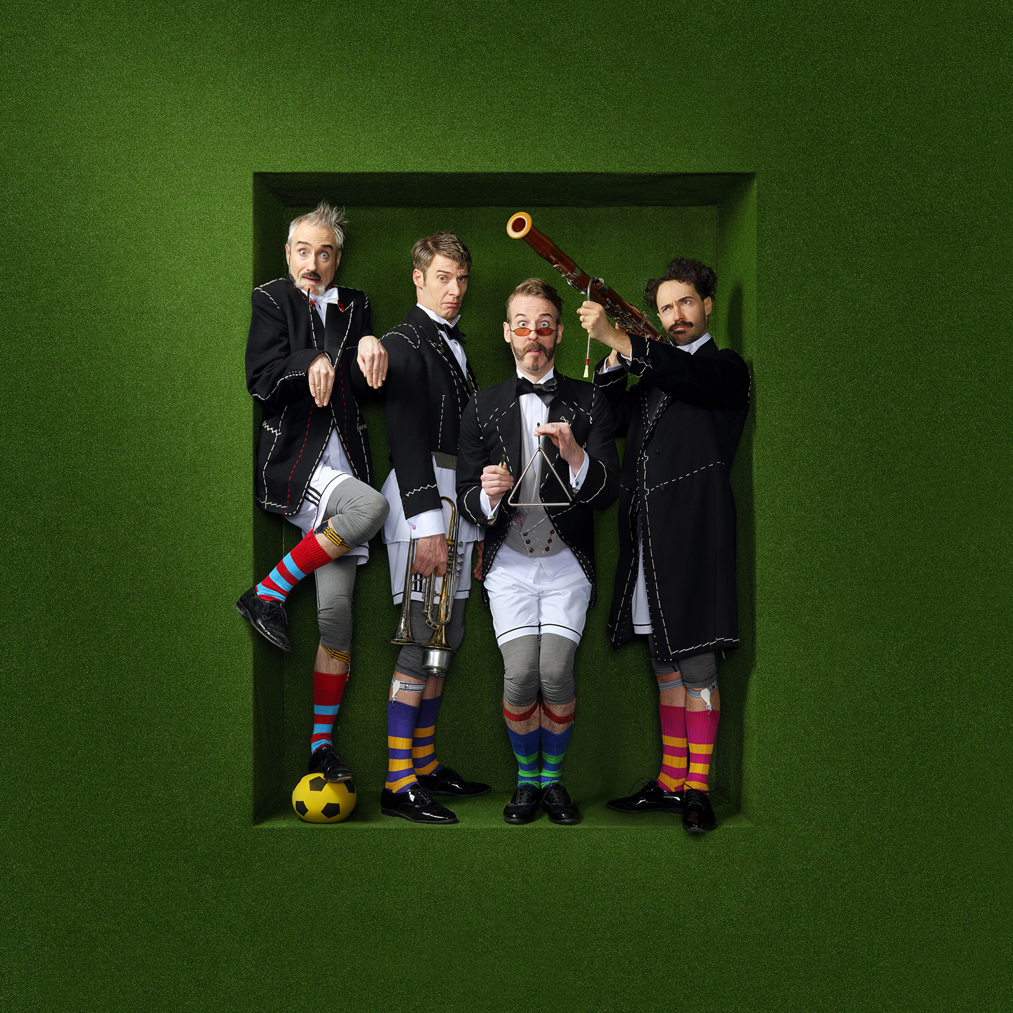 De muzikanten van Släpstick poseren met hun instrumenten, terwijl ze een uniform aan hebben met fel gekleurde en gestreepte sokken.