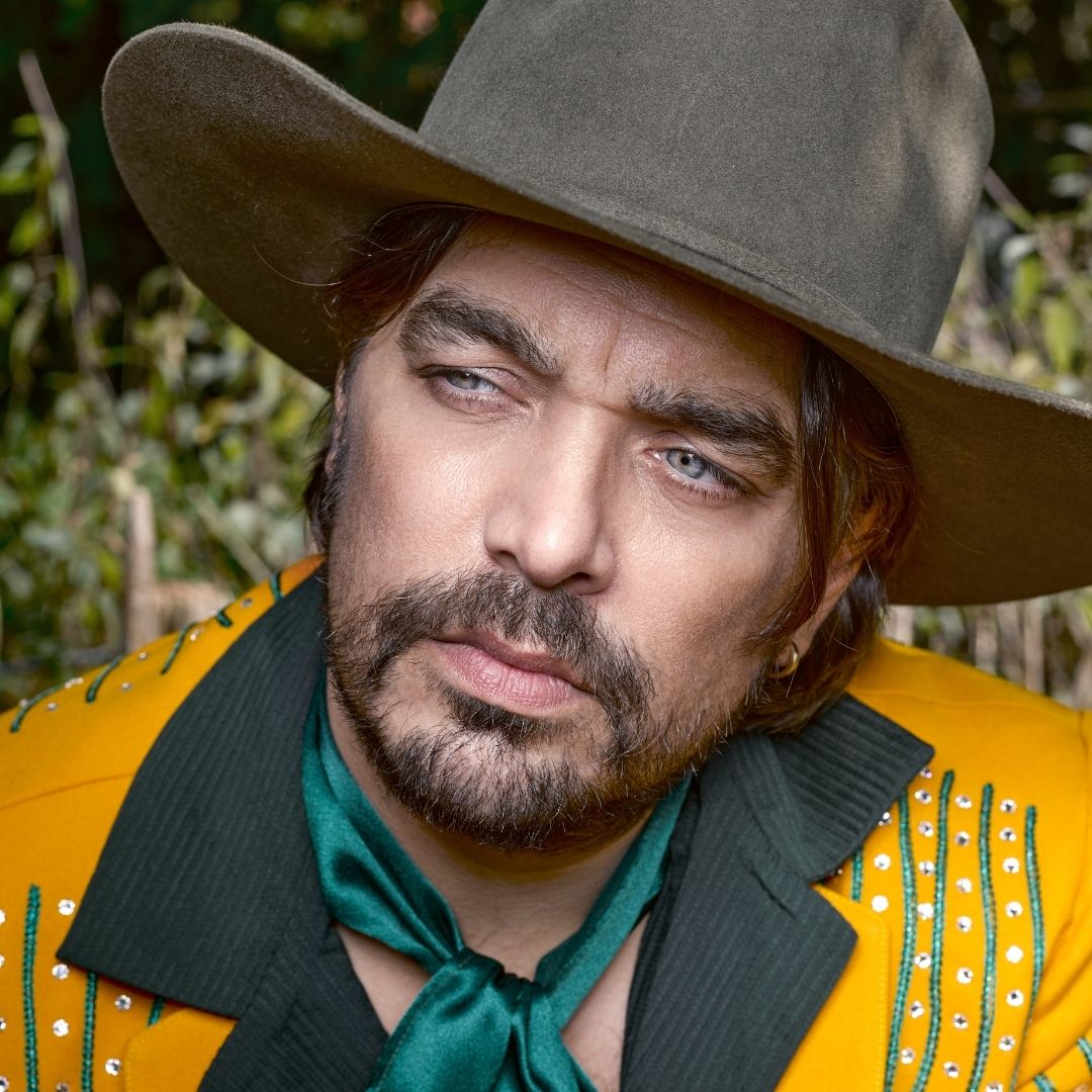 Waylon heeft een geel pak aan en een groene cowboyhoed.