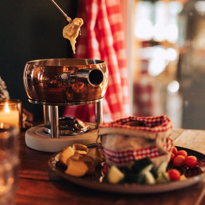 Een gezellig tafeltje met een pan kaasfondue erop omringd met groenten.