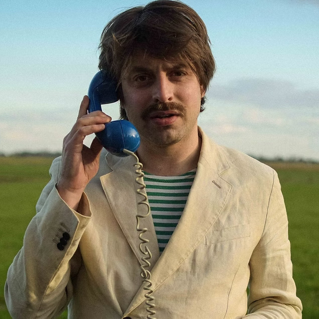 Joost Oomen houdt een blauwe telefoon aan zijn oor, midden in een open veld.