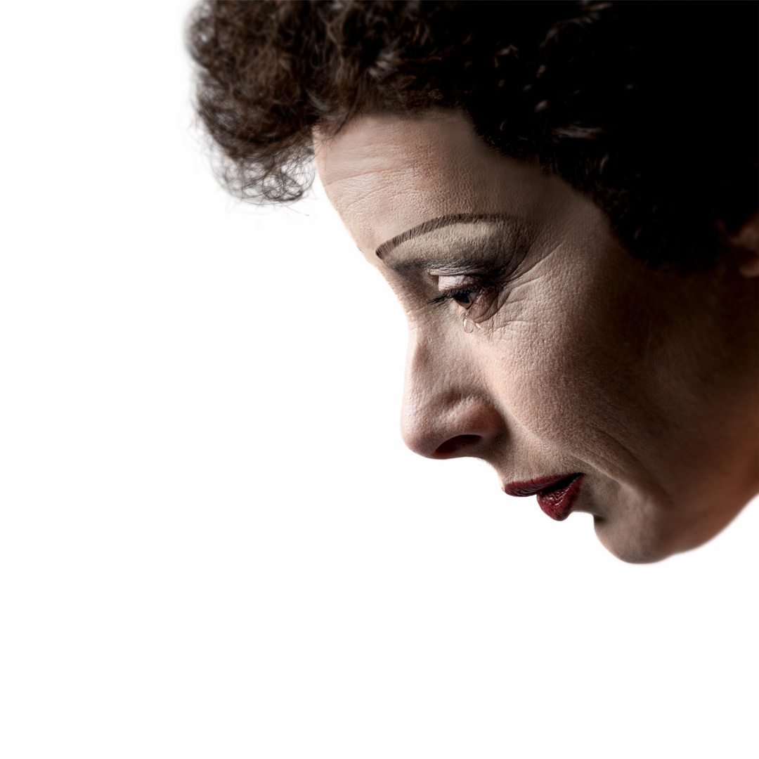 Piaf met traan op haar wang kijkt omlaag tegen witte achtergrond.