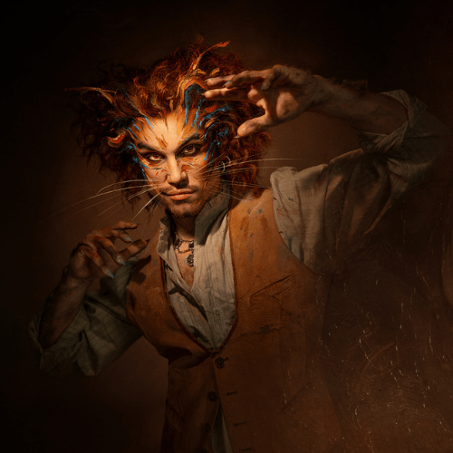 Je ziet een Cats-acteur met kattenmake-up en opgeheven handen in klauwpose onder warm licht.