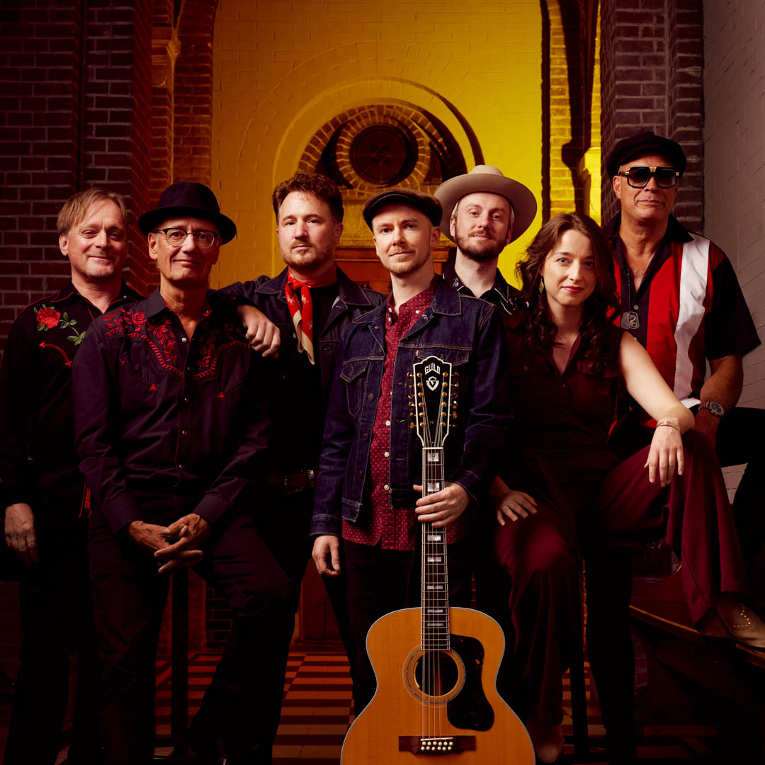 Band poseert met gitaar in Rocky Mountain High - a Tribute to John Denver onder warm podiumlicht.