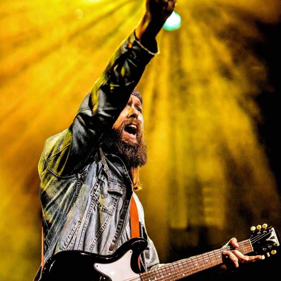 Gitarist met opgeheven arm onder gele spotlights op het Bluesfestival in Stadstheater Zoetermeer.
