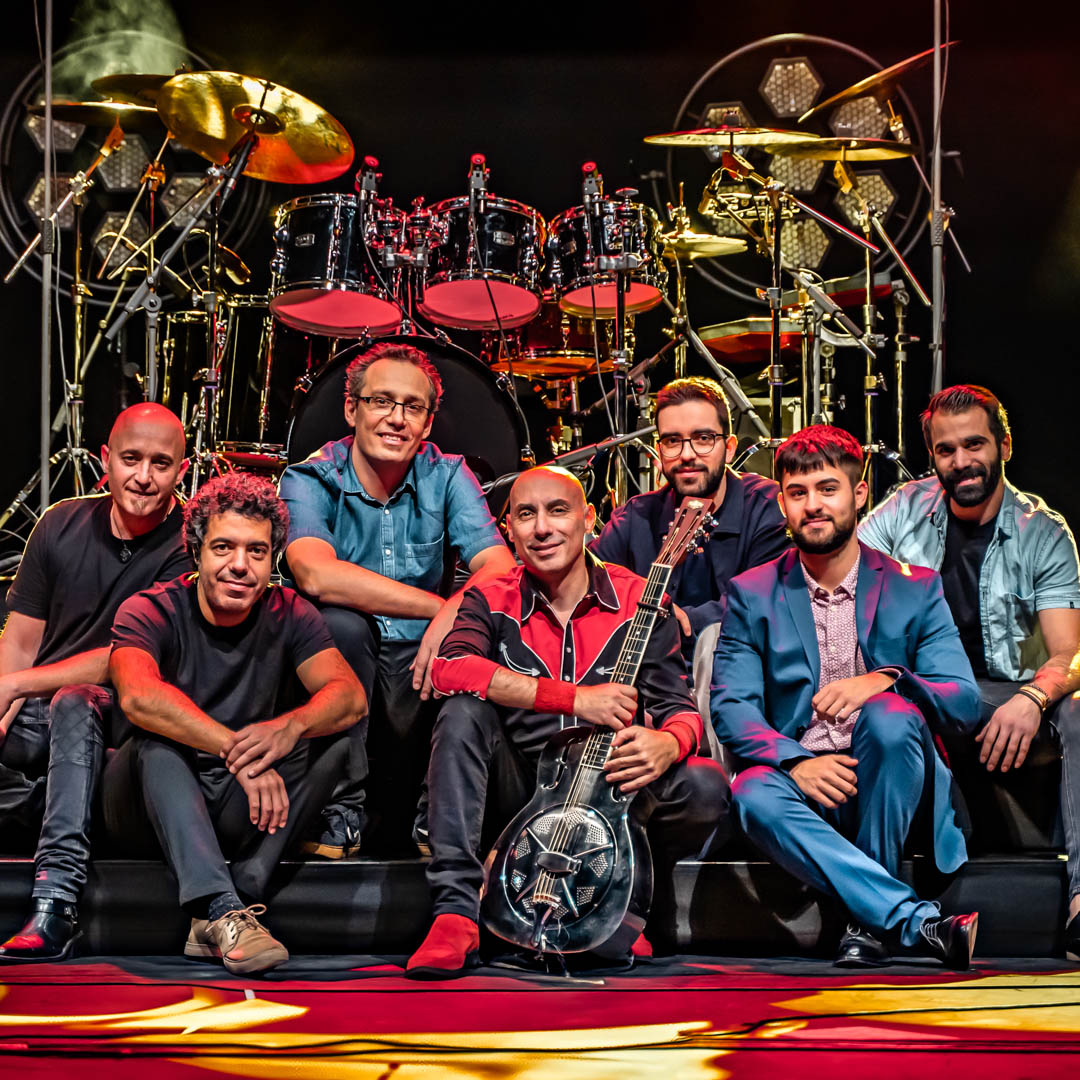 Bandleden zitten samen op podium in Brothers in Band - Ode aan de Dire Straits met gitaren en drumstel.