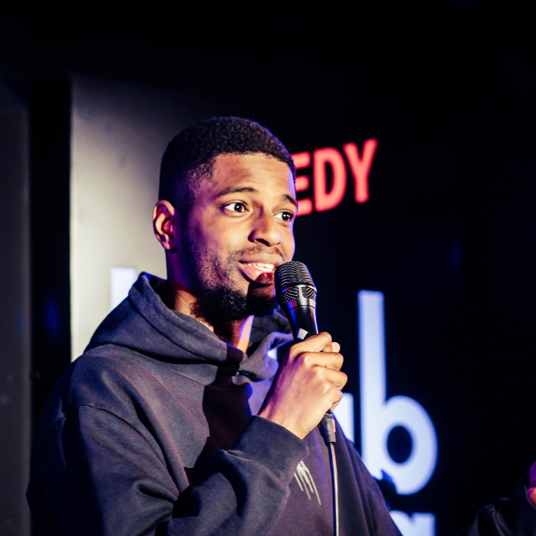 Comedian in donker voor neon comedy club logo in Comedy Club Haug.