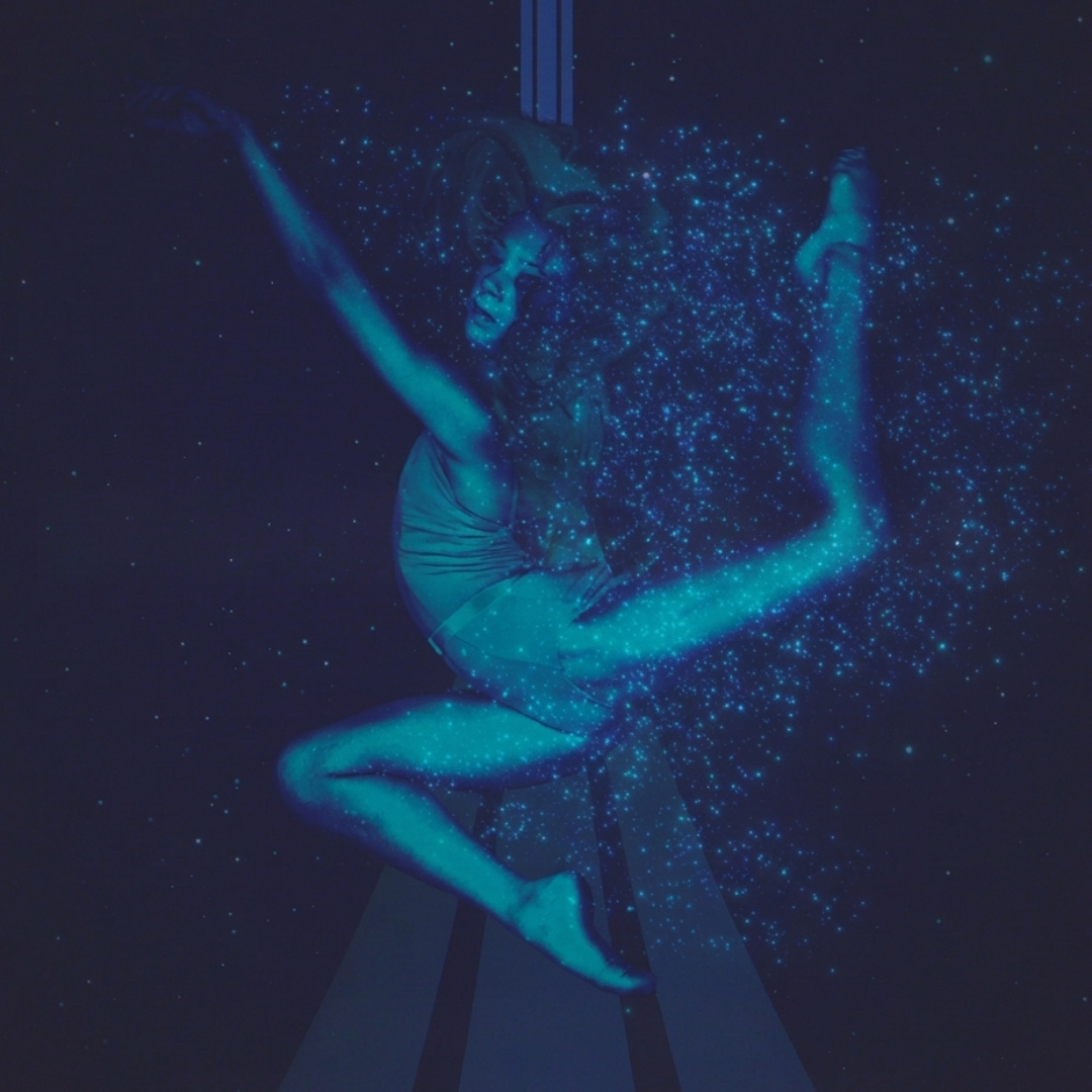 Danseres zweeft in de lucht aan doeken, omgeven door blauwe lichtpuntjes in Proxima van Degas International Dance Academy.
