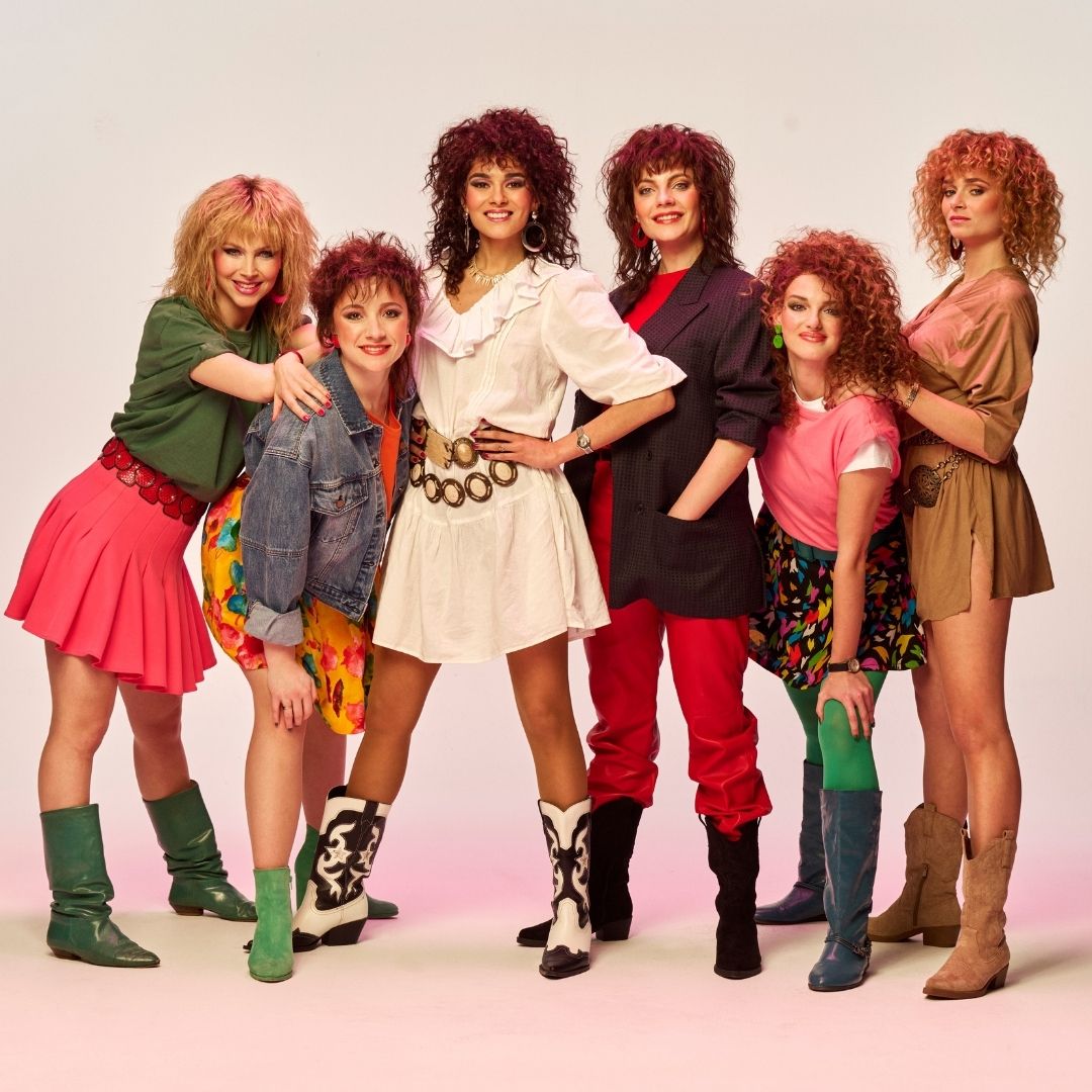 Zangeressen stralen in Dolly Dots de musical met krullend haar en retro styling.