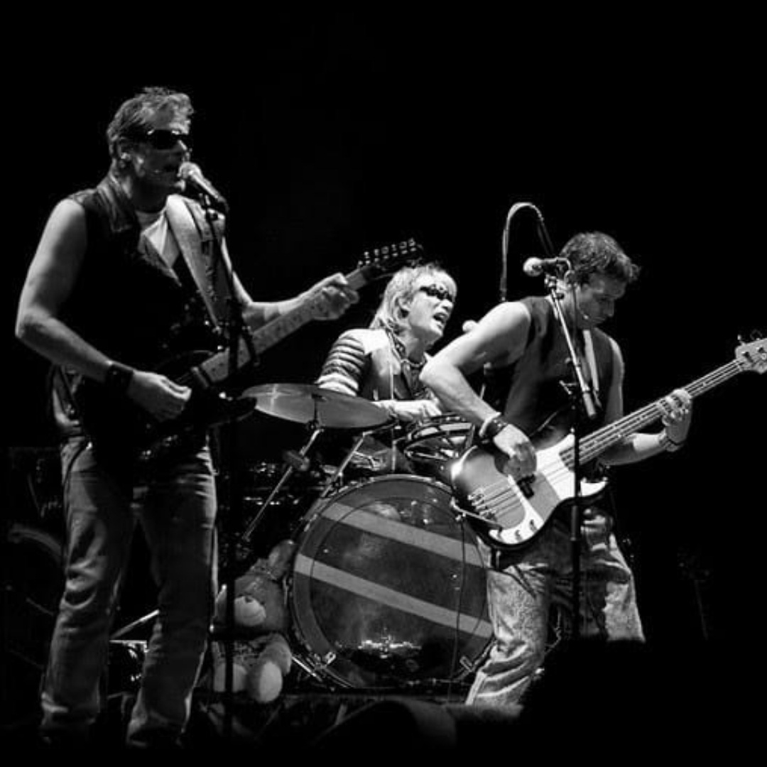 Drie muzikanten spelen live in Eigenlijk met gitaren en drumstel in zwart-wit.