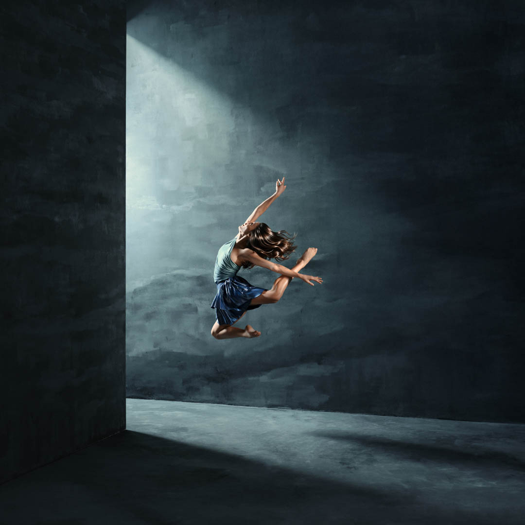 Danser maakt dynamische sprong onder lichtstraal op donker podium in Introdans Energy.