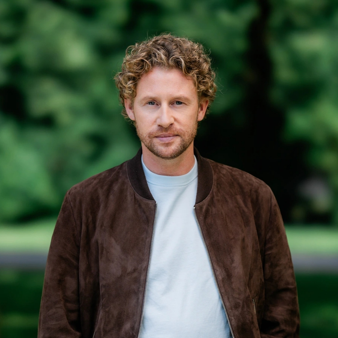 Ewout Genemans poseert in casual outfit met rustige blik in parkachtige omgeving.