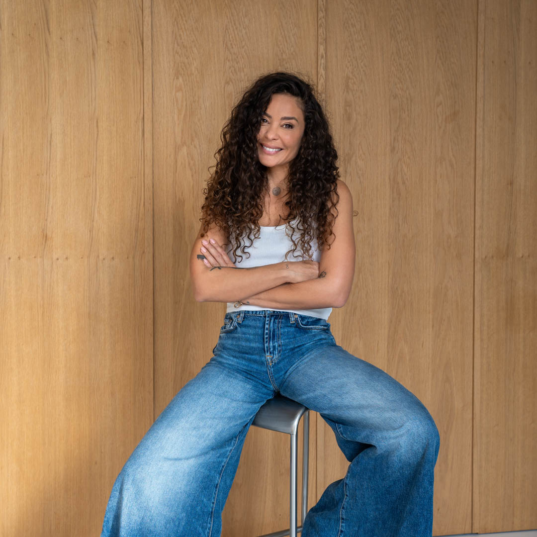 Fajah Lourens zit ontspannen op kruk met zelfverzekerde glimlach.