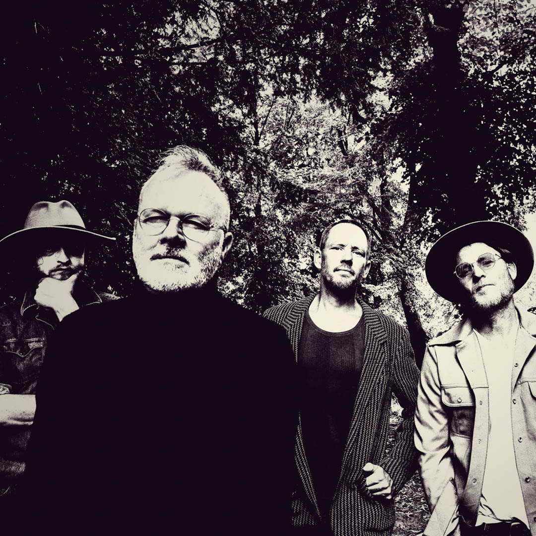 Bandleden staan samen in Her Majesty - Neil Young & Crazy Horse tussen hoge bomen in zwart-wit.