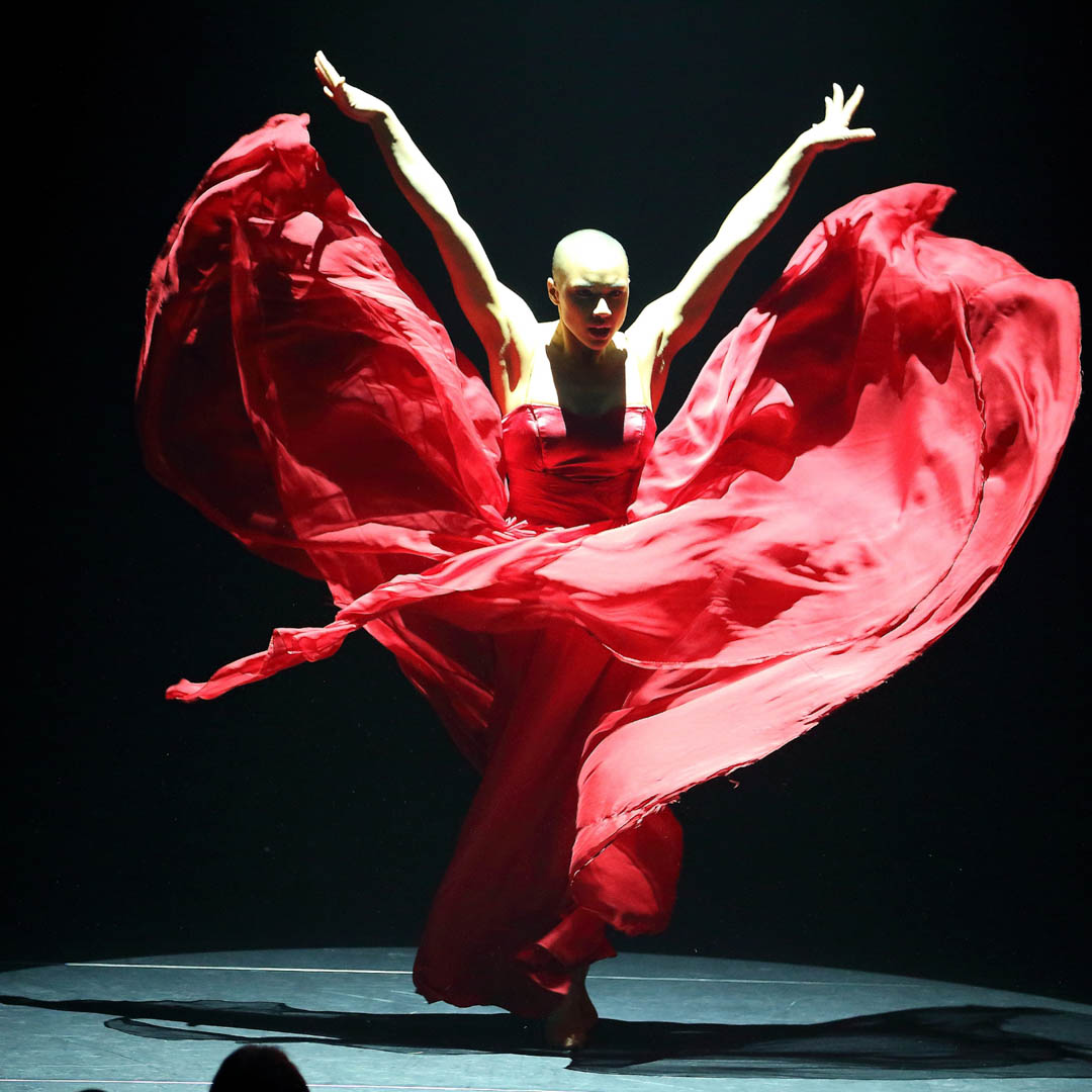 Danseres in rode jurk zweeft over het podium in dansvoorstelling Isabelle Beernaert Rouge.