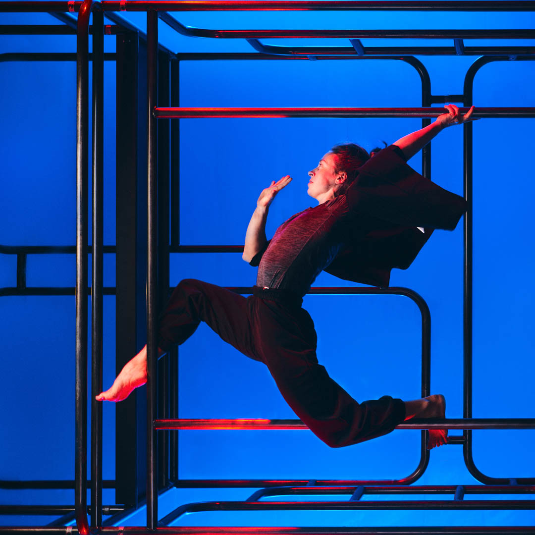 Danser springt krachtig in ISH Dance Collective - Rhythm & Flow tegen blauw grafisch decor.