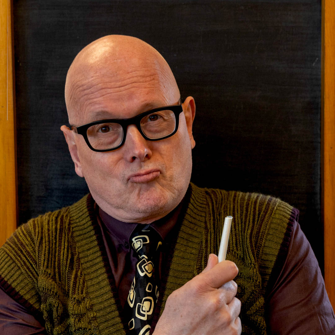 Kees van Amstel houdt een krijtje vast in Mogen we eerder weg? in klaslokaalsetting.