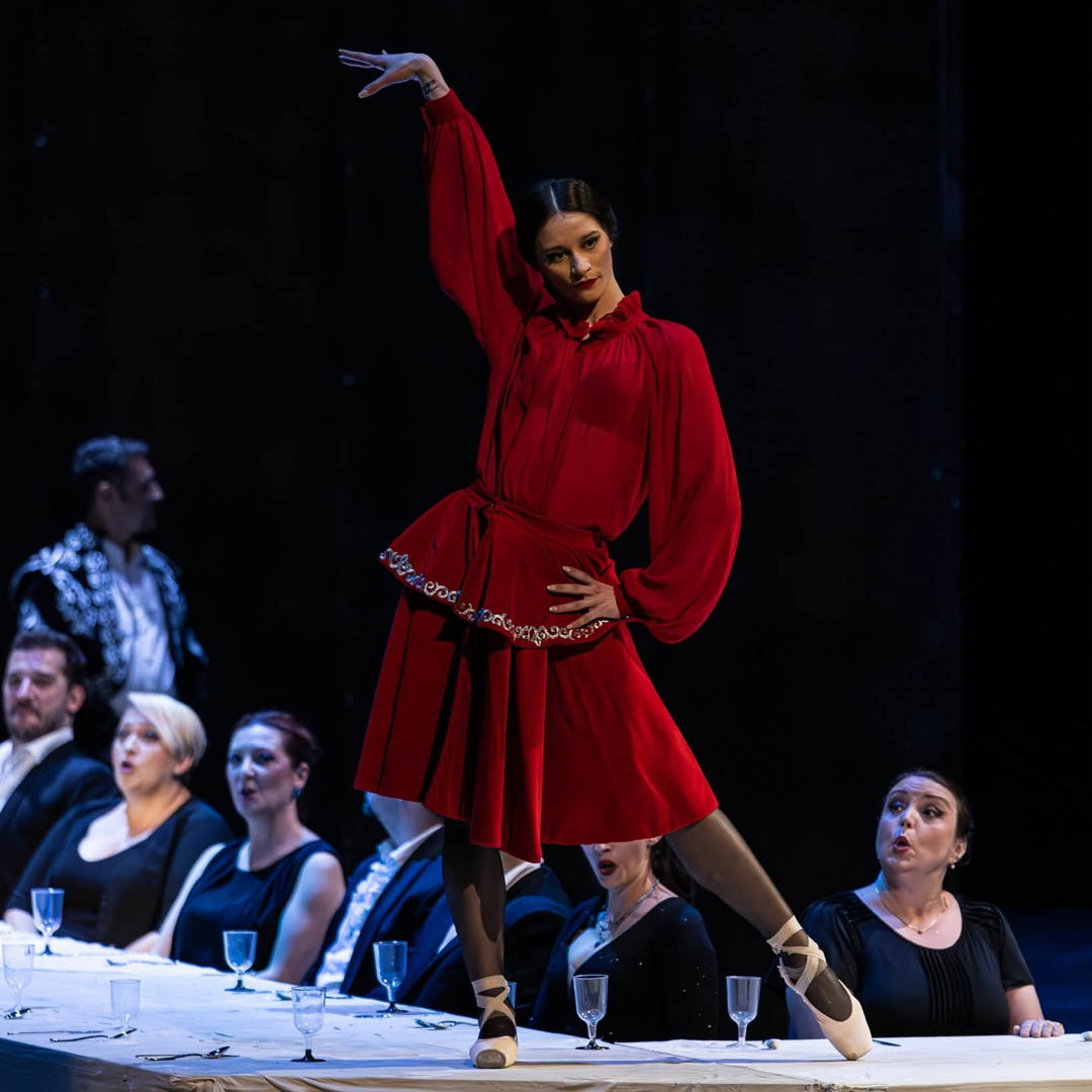 Sopraan in rode jurk danst op podium in operaproductie La Traviata.