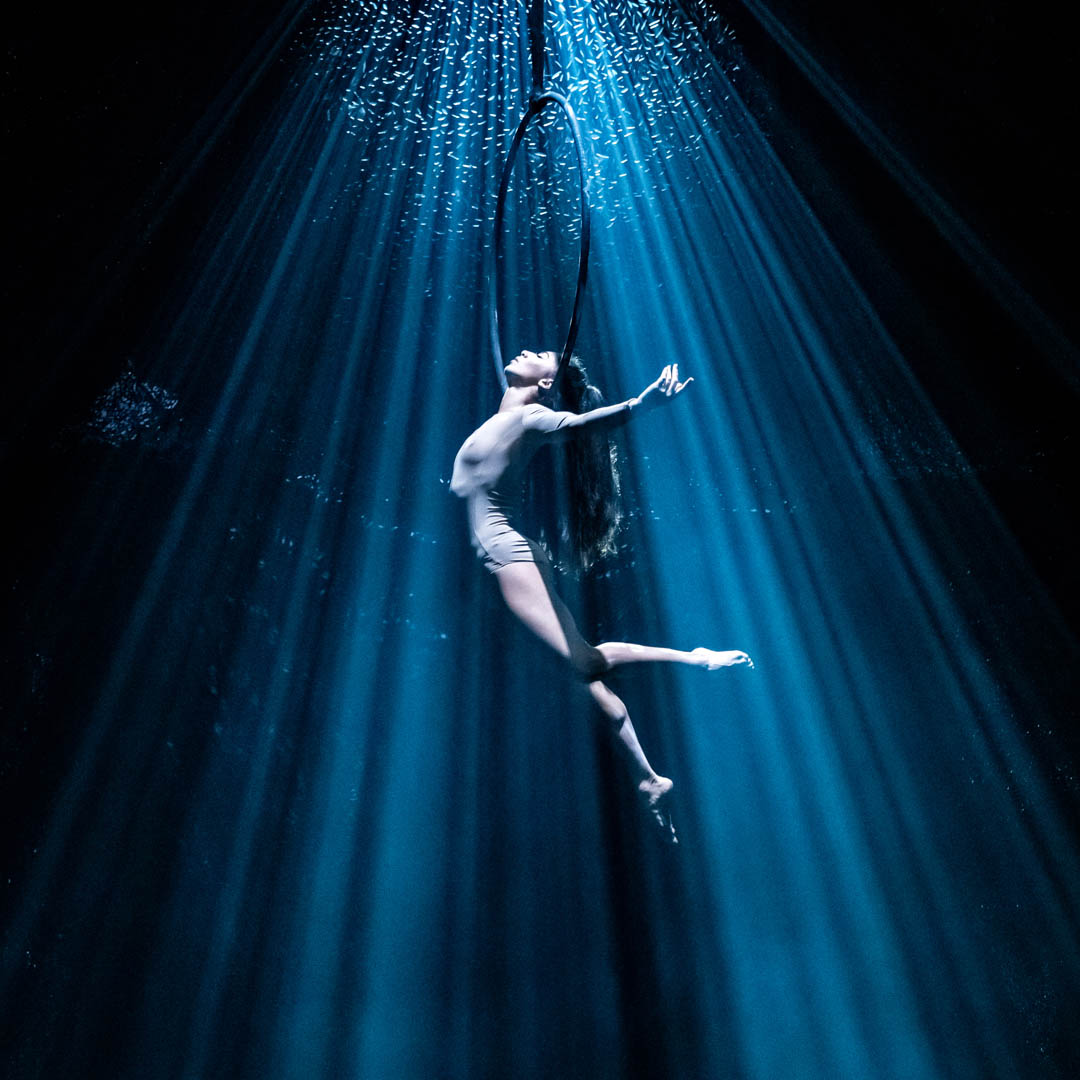 Acrobaat hangt in de lucht onder een lichtstraal in circusvoorstelling Recirquel Paradisium.