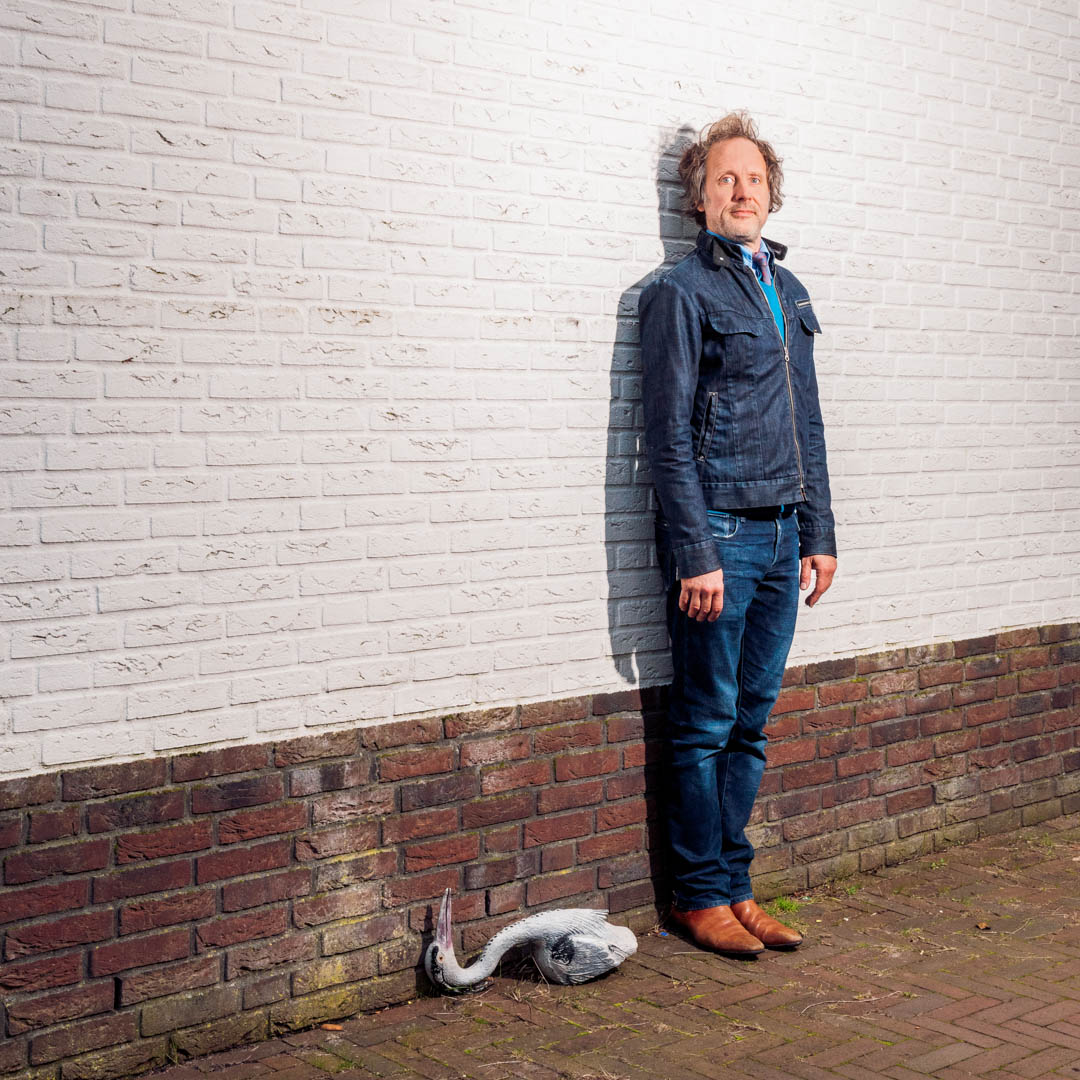 Ronald staat met plastic reiger naast een witte muur.