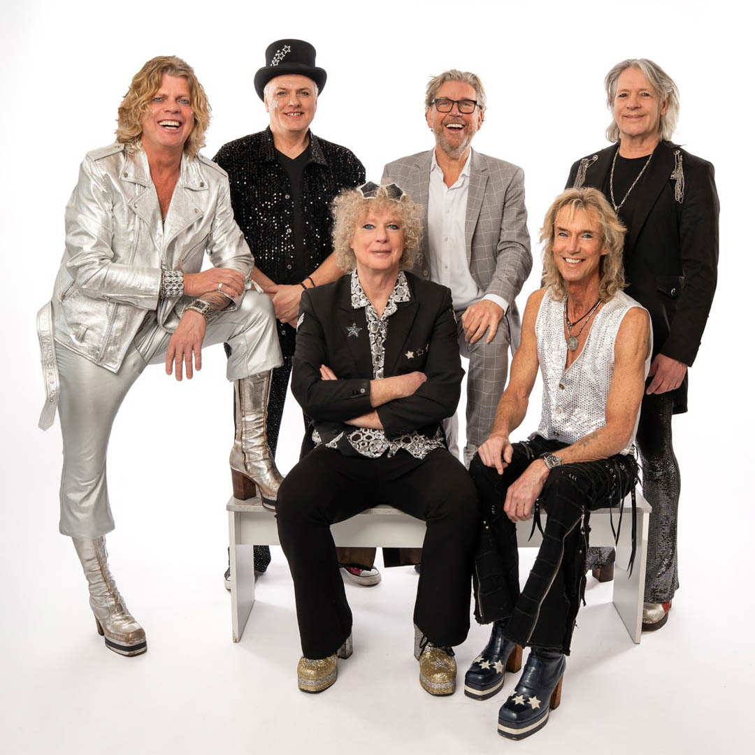 The Glamrocks staan zelfverzekerd bij elkaar in opvallende zilveren en zwarte kleding.