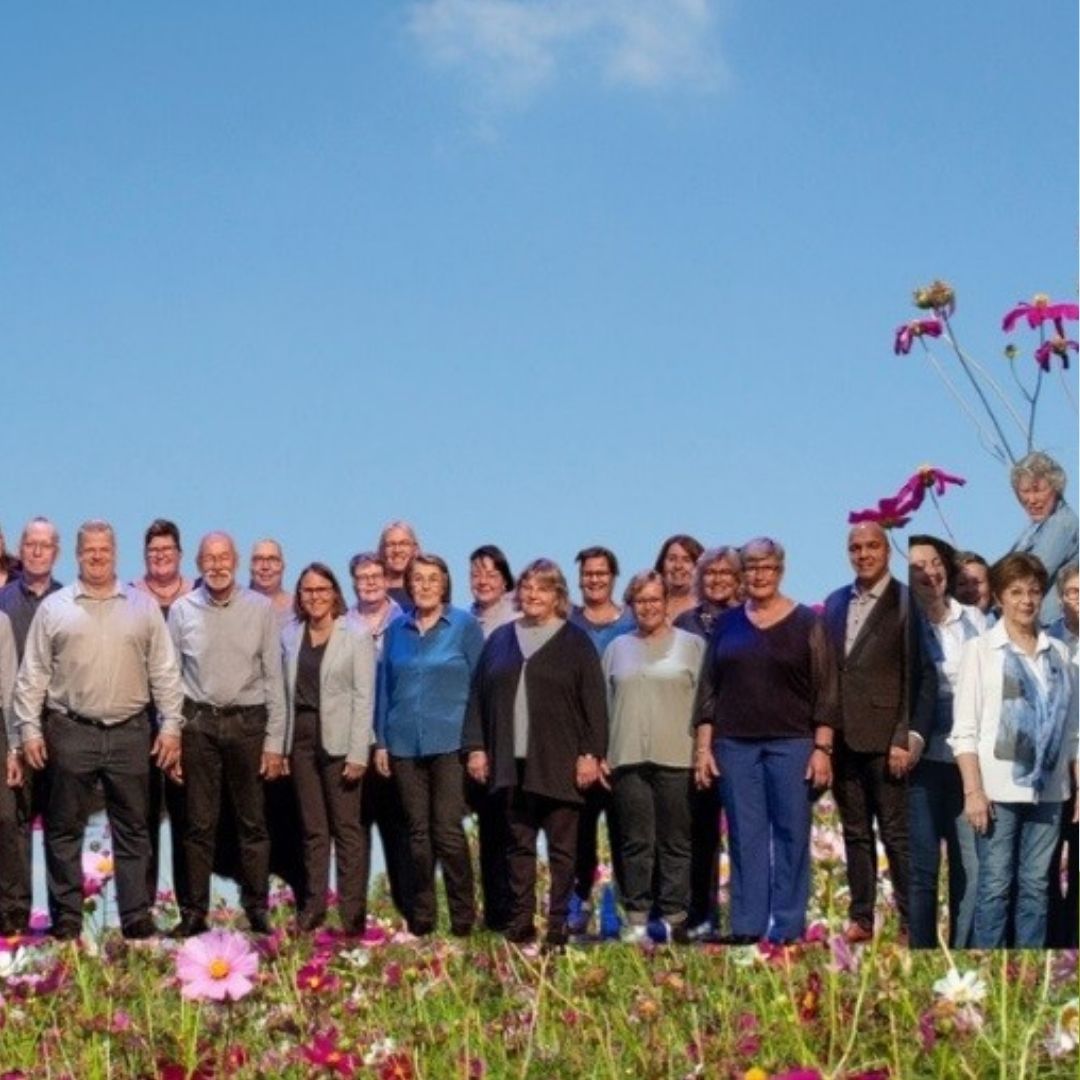 Koorleden van The Sprinter Singers en Total Praise staan in een kleurrijk bloemenveld onder een blauwe lucht.