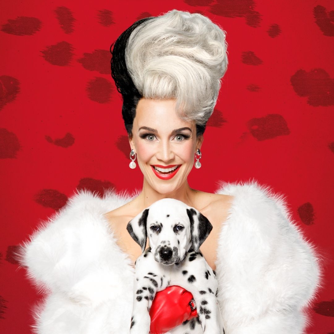 Cruella staat met dalmatiër in 101 Dalmatiërs de musical tegen rode achtergrond met vlekjes.