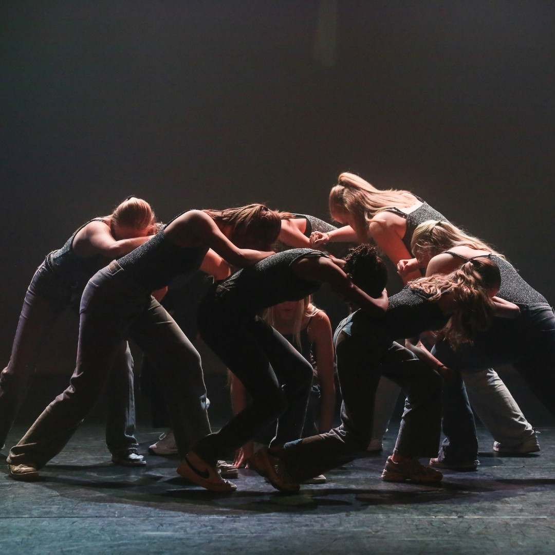 Groep dansers van Dansschool Devotion vormt een dichte kluwen op het podium, gebogen naar een middelpunt.