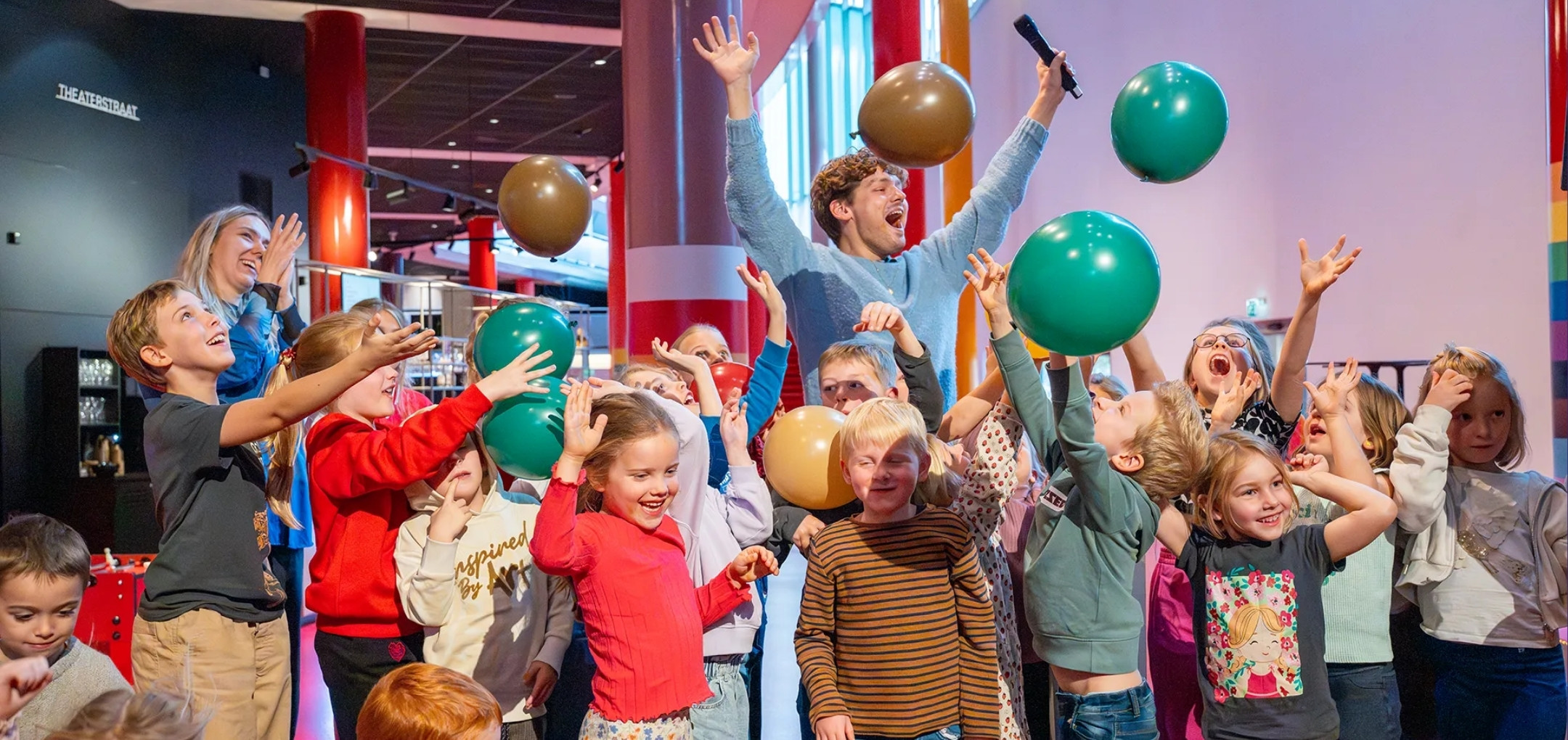Kinderen gooien gekleurde ballonnen omhoog in de foyer tijdens de Kindertheaterweek.