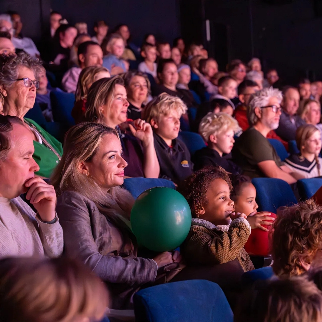 Volle theaterzaal met ouders en kinderen die aandachtig toekijken.