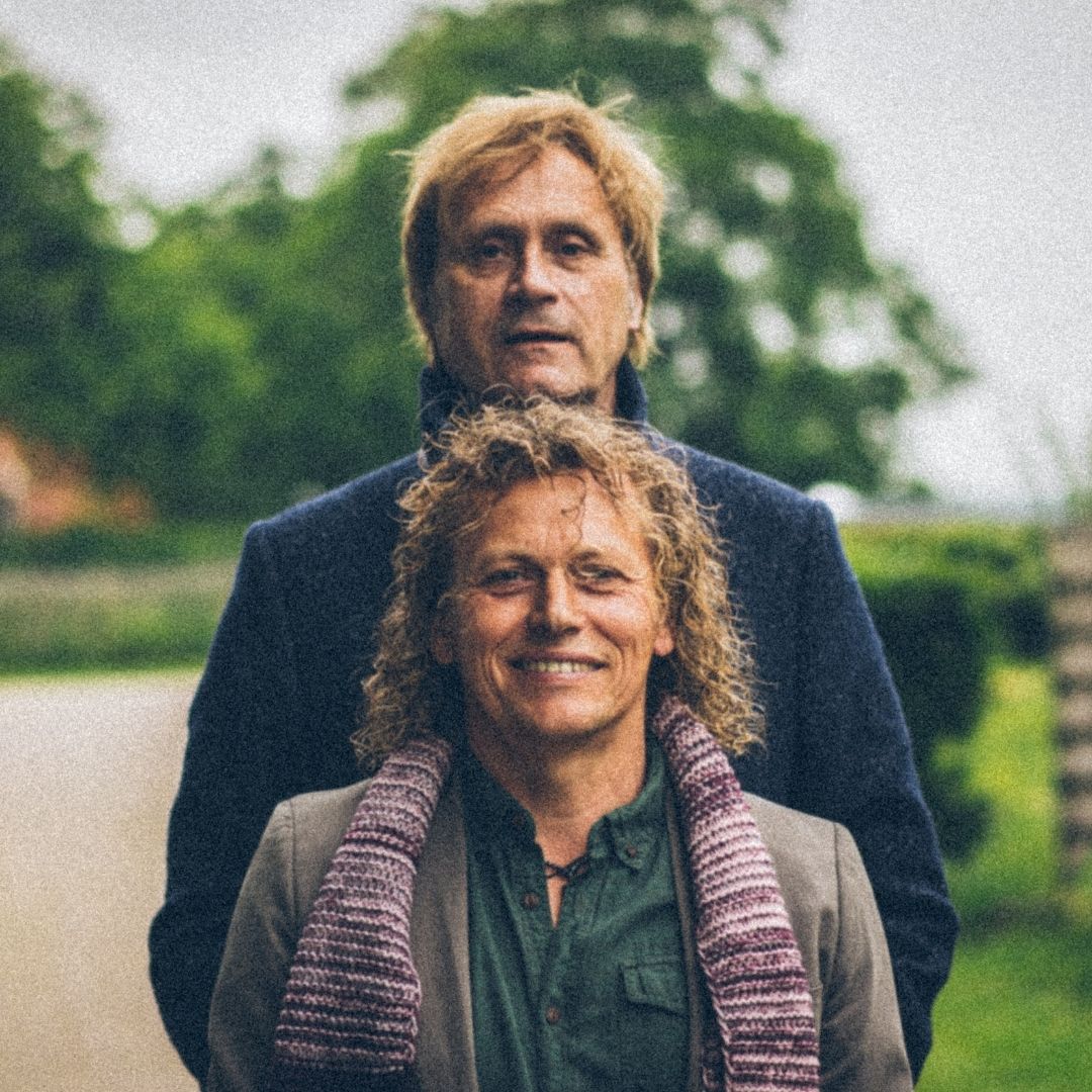 Twee muzikanten staan achter elkaar in een groene buitenomgeving voor The Best of Simon & Garfunkel.