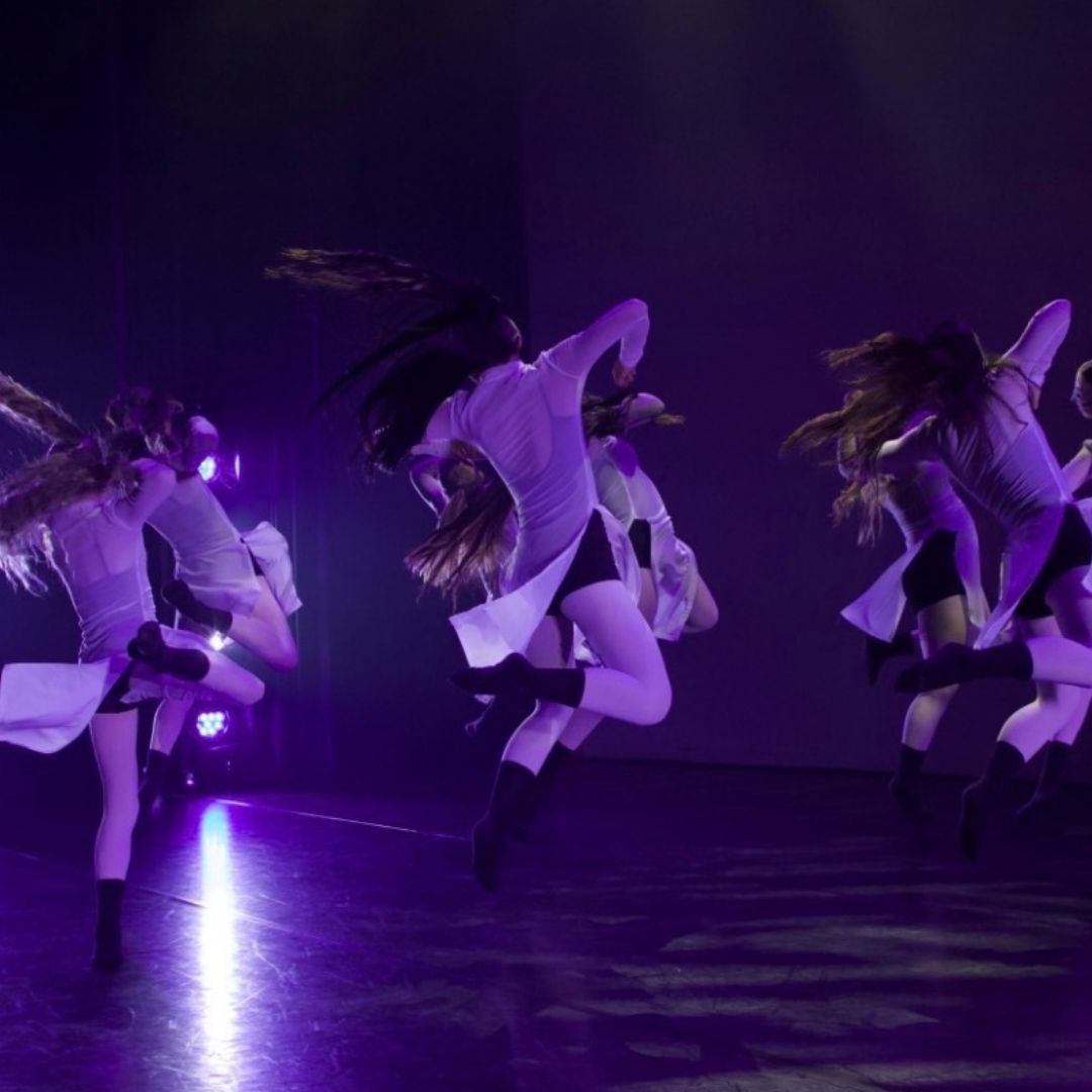 Meerdere dansers op het podium in paarse verlichting